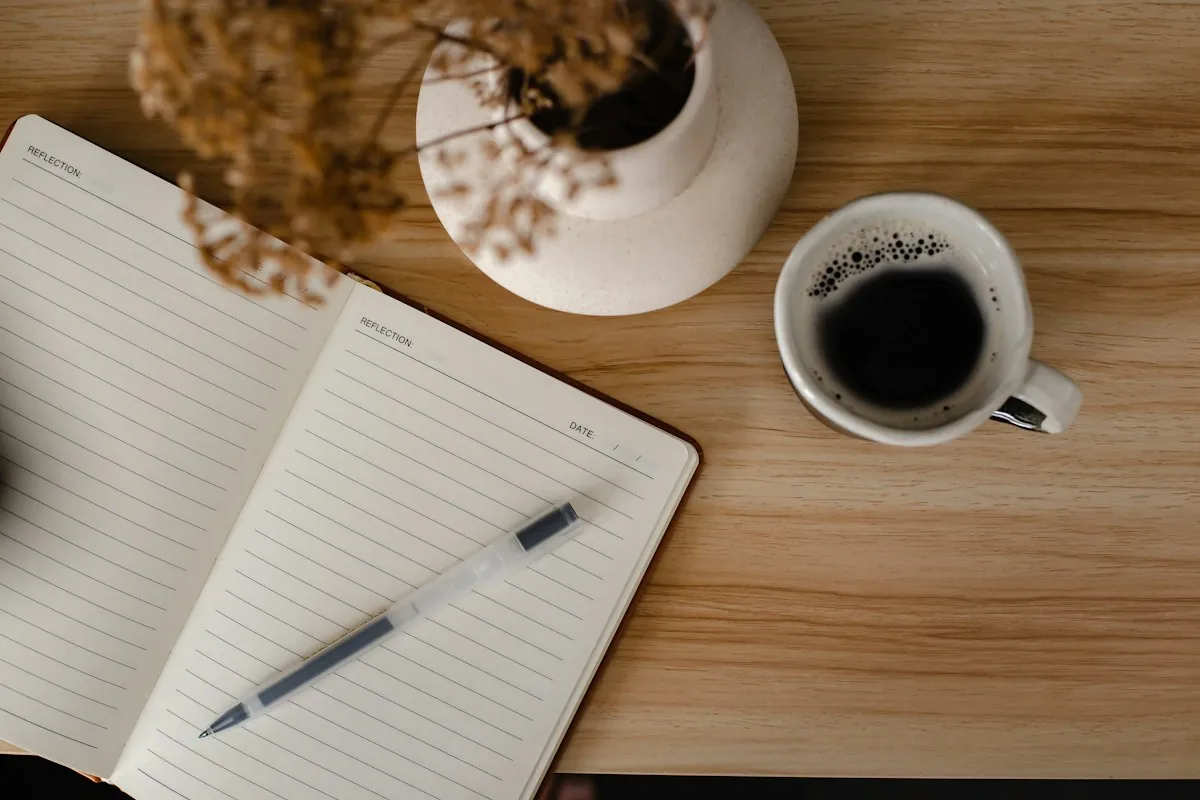An open notebook and pen beside a cup of coffee